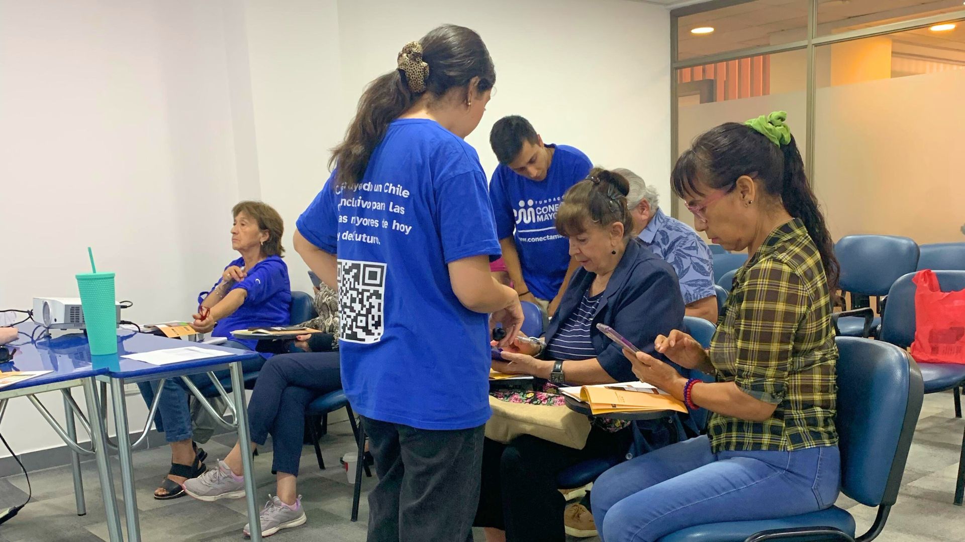 Clase de habilidades digitales a pensionados de Caja Los Andes. Dos relatores de Conecta Mayor UC trabajan con un grupo de 6 personas mayores, cada una tiene su teléfono en la mano.